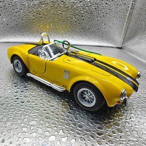 K&ouml;nnte beinhalten: Gelbes Spielzeugautomodell eines klassischen Sportwagens mit schwarzen Rennstreifen und einem silbernen Auspuff. Das Auto hat einen schwarzen Innenraum und eine klare Windschutzscheibe. Das Auto tr&auml;gt die Nummer 427 an der Seite.