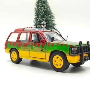 May include: A toy SUV, styled after the Jurassic Park film. The vehicle is painted yellow, green, and red, with the Jurassic Park logo on the side. The wheels are black and yellow. The SUV has a black front bumper and two black lights.