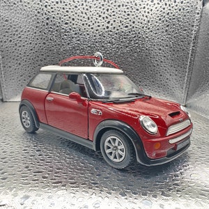 Peut inclure: Une décoration de voiture rouge Mini Cooper avec un toit blanc et une boucle argentée pour accrocher. La voiture a des roues noires et une calandre argentée.