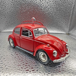 May include: A red vintage Volkswagen Beetle car ornament. The car has a silver bumper and chrome wheels. The ornament has a loop on top for hanging.