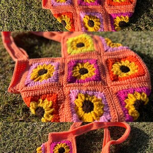 May include: A handmade crochet tote bag featuring a sunflower design. The bag is made of orange yarn with yellow, pink, and brown sunflower details. The bag has two handles and is sitting on green grass.