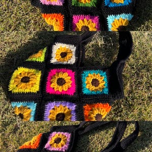 May include: Black crochet tote bag featuring colorful squares with sunflower designs. The sunflowers have yellow petals and brown centers, set against backgrounds of pink, green, blue, and orange. The bag has two black handles.