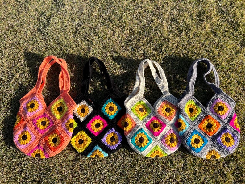 May include: Four handmade crochet tote bags with sunflower designs. Each bag features a different color scheme: orange, black, white, and gray. The bags are made with colorful squares and have matching handles.