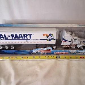 May include: A Kenworth W900 semi-truck model in a box, featuring Walmart and Sam's Club branding. The trailer is white with blue text. A yellow measuring tape placed in front shows the box length is approximately 19 inches long in total.