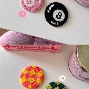 May include: Four colorful, round coasters with a textured, tufted design. One is pink with a white 8-ball design, another is black with a white 8-ball design, a third is yellow and red checkered, and the last is green and yellow checkered.