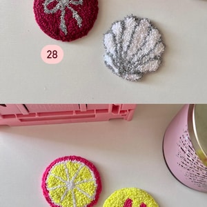 May include: A collection of colorful, circular, embroidered patches. Designs include a red circle with a silver bow, a white and silver seashell, a lemon slice, and a yellow smiley face with pink details. The number 28 and 29 are visible.