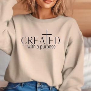 May include: A beige sweatshirt with a black cross and the text "CREATED with a purpose".