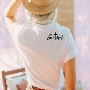 May include: White t-shirt with a black cross and the word "Grateful" written in cursive.