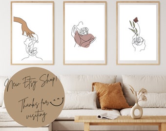 May include: Three minimalist line art prints in wooden frames, featuring abstract designs of hands, a flower, and a head. The prints are hung on a white wall above a beige couch with a brown throw pillow.