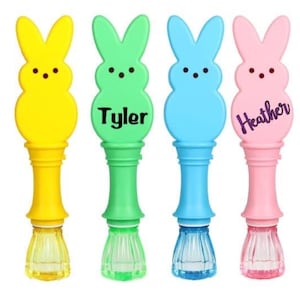 May include: Four colorful bubble wands shaped like Easter bunnies. The wands are yellow, green, blue, and pink, each with a different colored handle and base. The green wand has the name "Tyler" and the pink wand has the name "Heather".