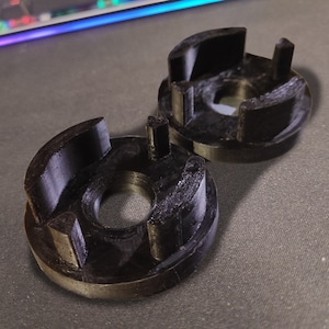 Könnte beinhalten: Zwei schwarze, 3D-gedruckte Ringe aus Kunststoff mit einem runden Loch in der Mitte und vier gleichmäßig verteilten Laschen um das Loch.