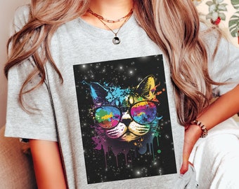 May include: A grey t-shirt with a colourful cat wearing sunglasses. The cat design is a vibrant mix of colours, set against a black background with sparkling stars. The shirt is a casual, everyday wear item.