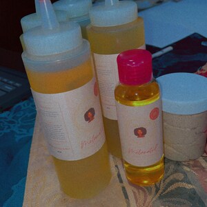 May include: Several clear plastic squeeze bottles with red caps and labels, filled with a yellow liquid. A small glass bottle with a pink cap and a jar with a light blue lid are also present. The labels feature a woman's face and the word "Melanated".
