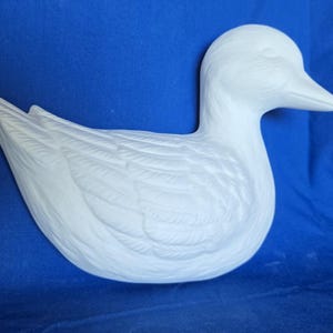 May include: A white ceramic duck figurine with detailed feather markings. The duck has a long neck and a small beak.