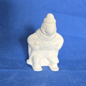 May include: White ceramic figurine of a person wearing a hat and scarf, sitting in a sled. The figurine is ready to be painted.
