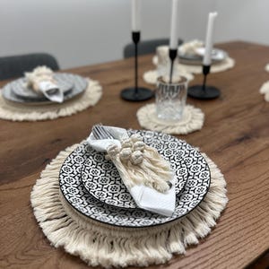 May include: A dining table set with black and white patterned plates, white napkins, and macrame placemats. The table is set with candles in black candle holders, creating an elegant and stylish aesthetic.