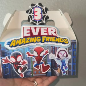 Puede incluir: Una caja de regalo blanca con el texto "EVER and his AMAZING FRIENDS". La caja est&aacute; decorada con im&aacute;genes de dibujos animados de personajes de Spider-Man y un n&uacute;mero 3 en un dise&ntilde;o de telara&ntilde;a.