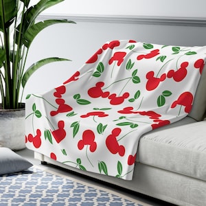 May include: White throw blanket with a red and green pattern of Mickey Mouse heads shaped like cherries.