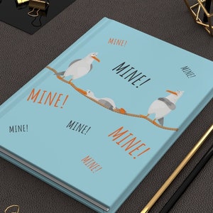 Peut inclure: Un carnet bleu clair avec un motif de mouettes sur une corde avec le mot "MINE!" r&eacute;p&eacute;t&eacute; plusieurs fois en texte orange.