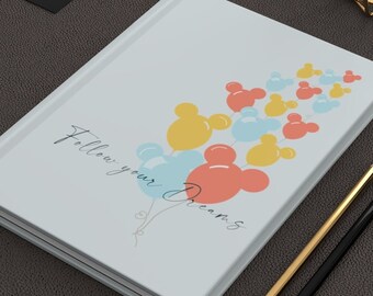 May include: A white journal with a light blue background and the text "Follow your Dreams" in black script. The journal features a design of colourful Mickey Mouse shaped balloons.