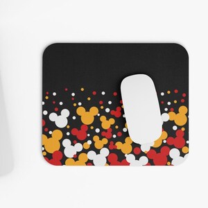 May include: Black mouse pad with a white mouse on top. The mouse pad has a pattern of red, yellow, and white Mickey Mouse heads on a black background.