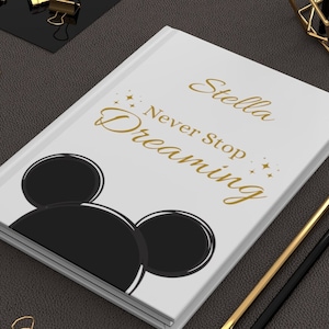May include: White notebook with a black Mickey Mouse silhouette and gold lettering that says "Stella Never Stop Dreaming".