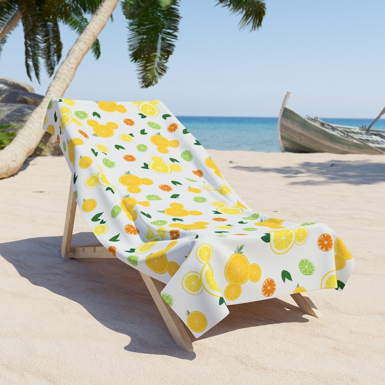 Puede incluir: Una silla de playa blanca con una toalla de playa con estampado de lim&oacute;n y lima. La toalla tiene un fondo blanco con limones amarillos, limas verdes y hojas verdes.