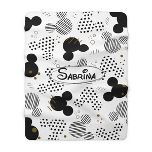 Puede incluir: Manta de franela blanca con un patr&oacute;n geom&eacute;trico en blanco y negro de cabezas de Mickey Mouse, lunares y rayas. El nombre Sabrina est&aacute; escrito en letras doradas en un c&iacute;rculo.