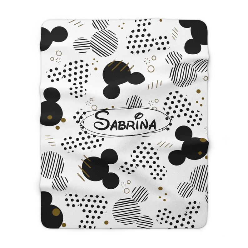 Puede incluir: Manta de franela blanca con un patr&oacute;n geom&eacute;trico en blanco y negro de cabezas de Mickey Mouse, lunares y rayas. El nombre Sabrina est&aacute; escrito en letras doradas en un c&iacute;rculo.