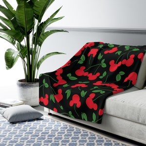 May include: A black fleece throw blanket with a red and green cherry pattern. The cherries are stylized to look like Mickey Mouse ears.