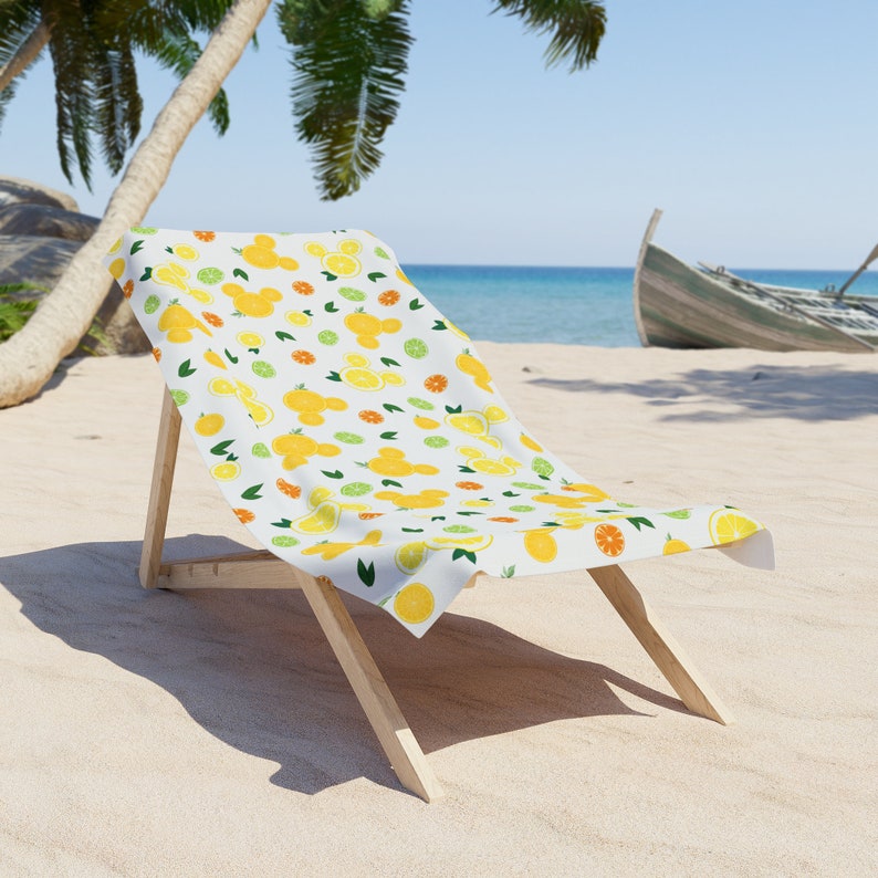 Puede incluir: Una silla de playa blanca con un patr&oacute;n de lim&oacute;n y lima. La silla est&aacute; hecha de madera y tiene un asiento de tela blanca. La silla est&aacute; en una playa de arena con un oc&eacute;ano azul en el fondo.