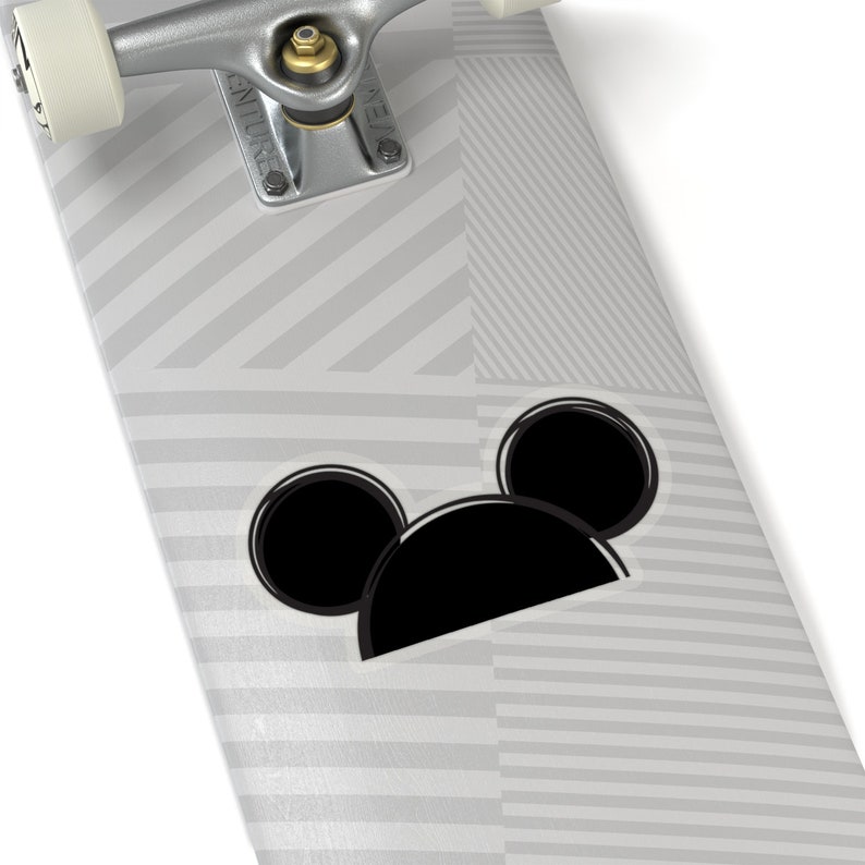 Op de afbeelding: Een wit skateboarddeck met een zwart-wit gestreept patroon. Een zwart-witte Mickey Mouse-kop sticker zit op het deck.