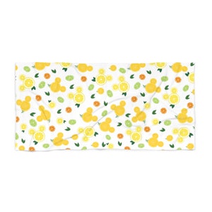 Puede incluir: Toalla de playa blanca con un patr&oacute;n repetido de rodajas de lim&oacute;n amarillo, hojas verdes y rodajas de c&iacute;tricos naranjas. Las rodajas de lim&oacute;n est&aacute;n dispuestas en forma de cabezas de Mickey Mouse.