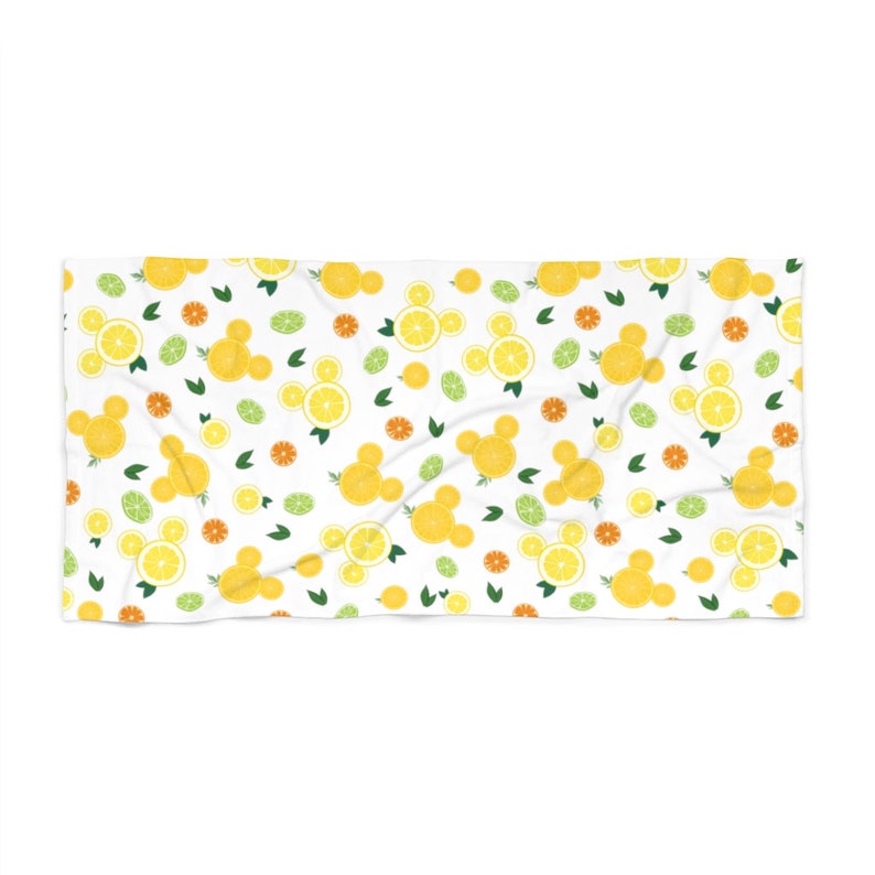Puede incluir: Toalla de playa blanca con un patr&oacute;n repetido de rodajas de lim&oacute;n amarillo, hojas verdes y rodajas de c&iacute;tricos naranjas. Las rodajas de lim&oacute;n est&aacute;n dispuestas en forma de cabezas de Mickey Mouse.