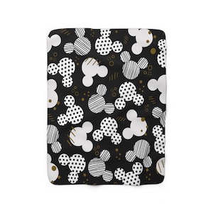Puede incluir: Manta de forro polar con estampado en blanco y negro con un dise&ntilde;o repetido de cabezas de Mickey Mouse. Las cabezas de Mickey Mouse est&aacute;n en varios patrones, incluyendo lunares, rayas y blanco s&oacute;lido.