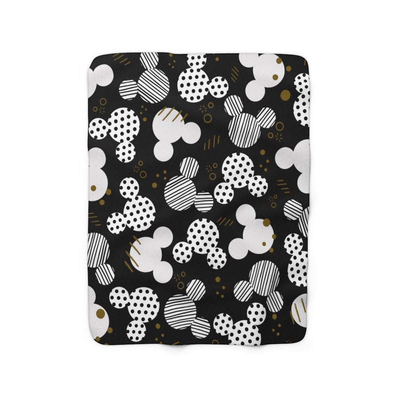 Puede incluir: Manta de forro polar con estampado en blanco y negro con un dise&ntilde;o repetido de cabezas de Mickey Mouse. Las cabezas de Mickey Mouse est&aacute;n en varios patrones, incluyendo lunares, rayas y blanco s&oacute;lido.
