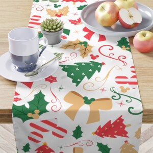 May include: White table runner with a Christmas theme featuring red and green Christmas trees, holly leaves, bows, candy canes, and Mickey Mouse heads.