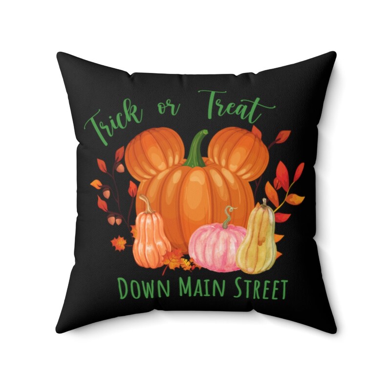 Puede incluir: Coj&iacute;n negro con un texto verde "Trick or Treat Down Main Street" y un gr&aacute;fico de una calabaza con orejas de Mickey Mouse rodeada de calabazas m&aacute;s peque&ntilde;as y hojas de oto&ntilde;o.