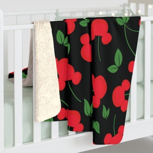 May include: A black fleece throw blanket with a red and green pattern of cherries. The cherries have a Mickey Mouse ear shape.