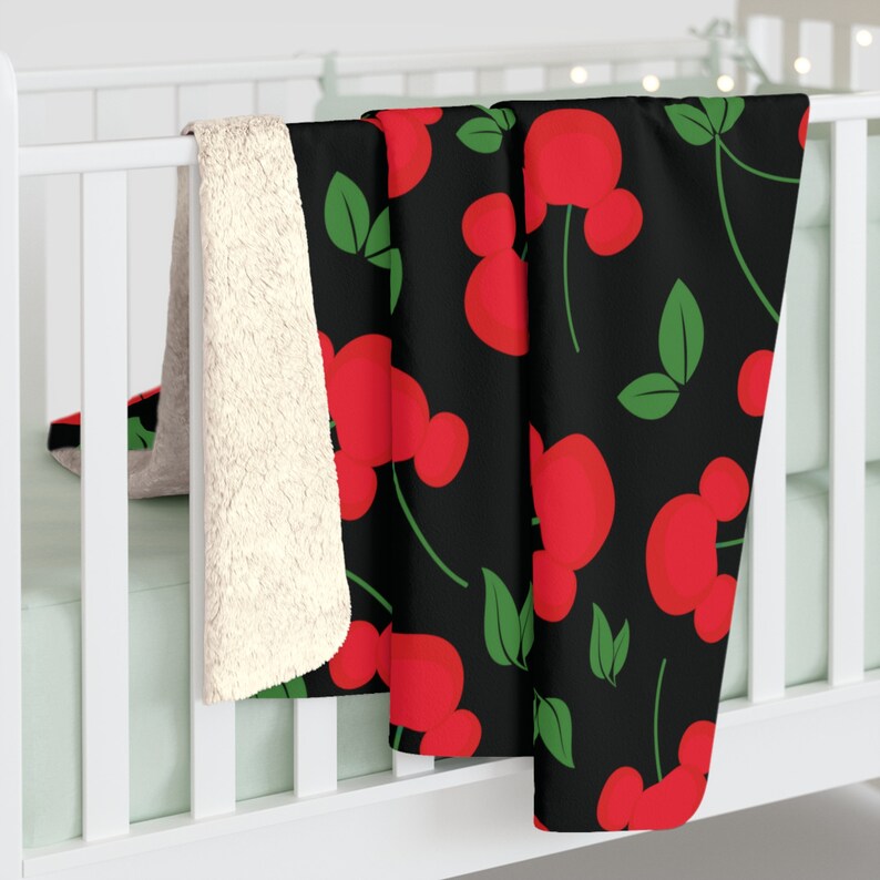 May include: A black fleece throw blanket with a red and green pattern of cherries. The cherries have a Mickey Mouse ear shape.