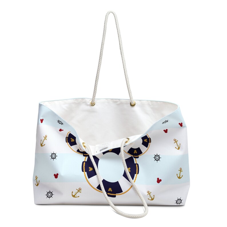 K&ouml;nnte beinhalten: Eine wei&szlig;e Canvas-Tragetasche mit blau-wei&szlig;en Streifen und nautischem Thema. Die Tasche zeigt einen Rettungsring mit Mickey-Maus-Ohren, Ankern und Schiffsr&auml;dern. Die Tasche hat wei&szlig;e Seilgriffe.