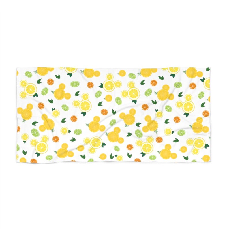 Puede incluir: Una toalla de playa blanca con un patr&oacute;n repetido de rodajas de lim&oacute;n amarillo, hojas verdes y rodajas de c&iacute;tricos naranjas. Las rodajas de lim&oacute;n est&aacute;n dispuestas en forma de cabezas de Mickey Mouse.
