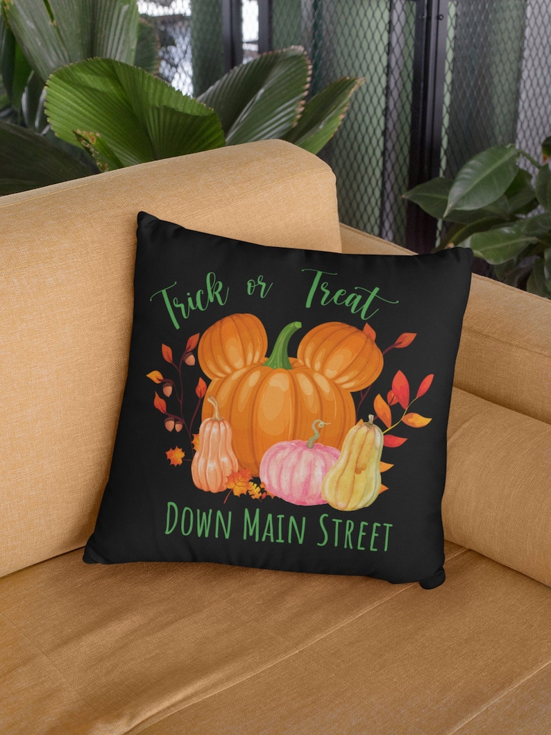 Puede incluir: Coj&iacute;n negro con texto blanco "Trick or Treat" y una cabeza de Mickey Mouse verde con calabazas y hojas de oto&ntilde;o. El texto debajo de la cabeza de Mickey Mouse dice "Down Main Street".