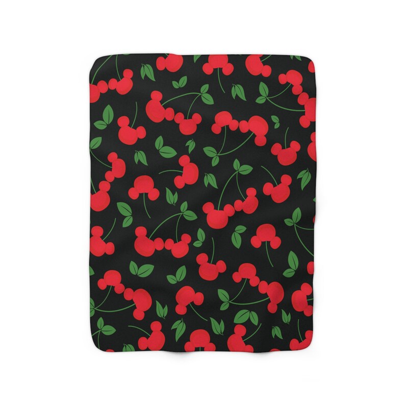 May include: A black and red patterned fleece blanket with a repeating pattern of red cherries with green stems and leaves. The cherries are shaped like Mickey Mouse ears.