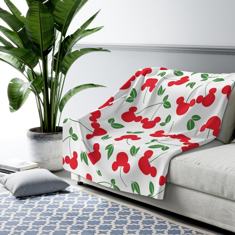 May include: White throw blanket with a red and green pattern of Mickey Mouse heads shaped like cherries.