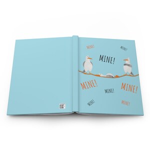 Peut inclure: Un livre ouvert avec une couverture bleue. Les pages int&eacute;rieures pr&eacute;sentent une illustration de cartoon de mouettes sur une corde avec le mot "MINE!" r&eacute;p&eacute;t&eacute; plusieurs fois.