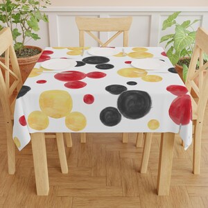 May include: A white tablecloth with a Mickey Mouse pattern. The pattern features red, yellow, and black watercolor circles.