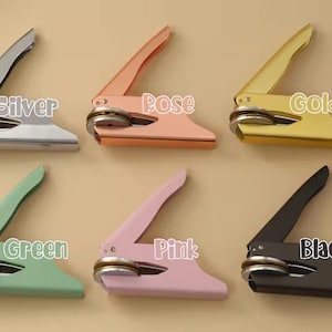 May include: Six metal seal presses in silver, rose, gold, green, pink, and black. Each press has a lever and a circular base, designed for creating embossed seals. The colour of each press is labelled on the image.