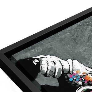 May include: Black and white framed canvas print of a hand reaching out with colorful dots on the hand and arm. The background is a textured gray.