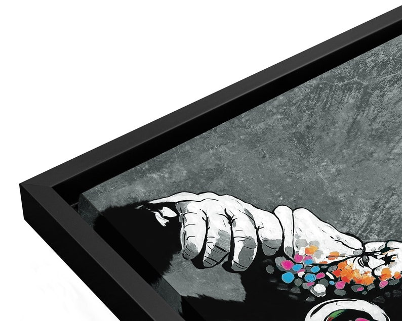 May include: Black and white framed canvas print of a hand reaching out with colorful dots on the hand and arm. The background is a textured gray.
